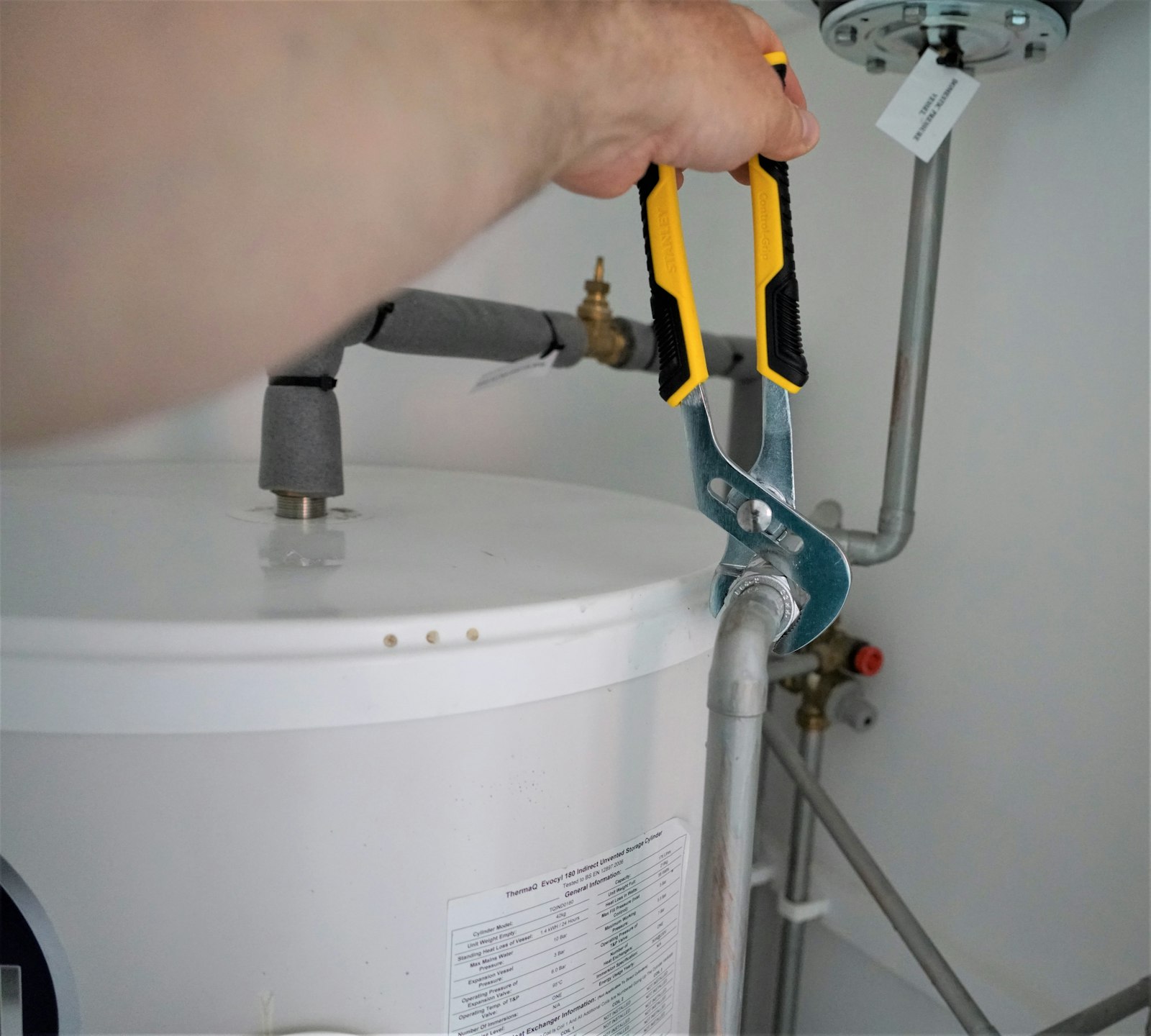 Plumber servicing a water heater cylinder with adjustable pliers